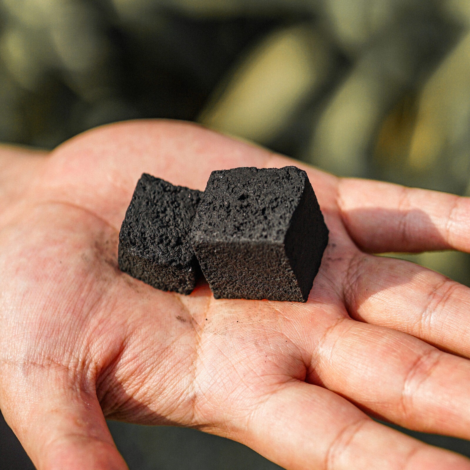 Two Cube Shaped Coconut Charcoals On A Hand