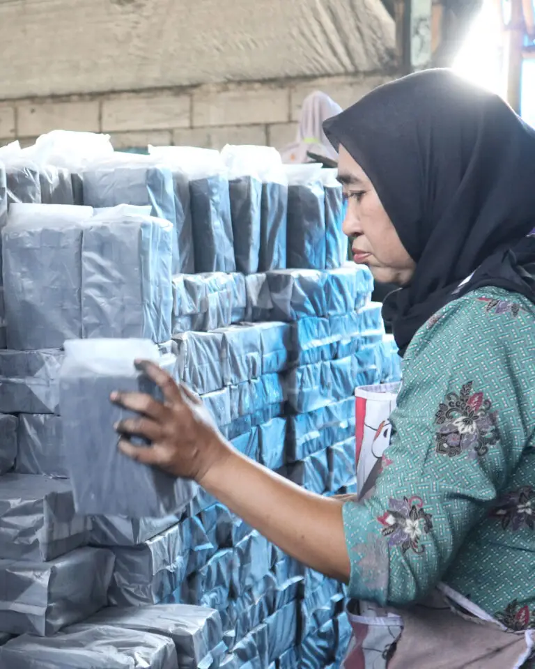 Indonesian Woman Stacking Packs of Coconut Charcoals In The Warehouse